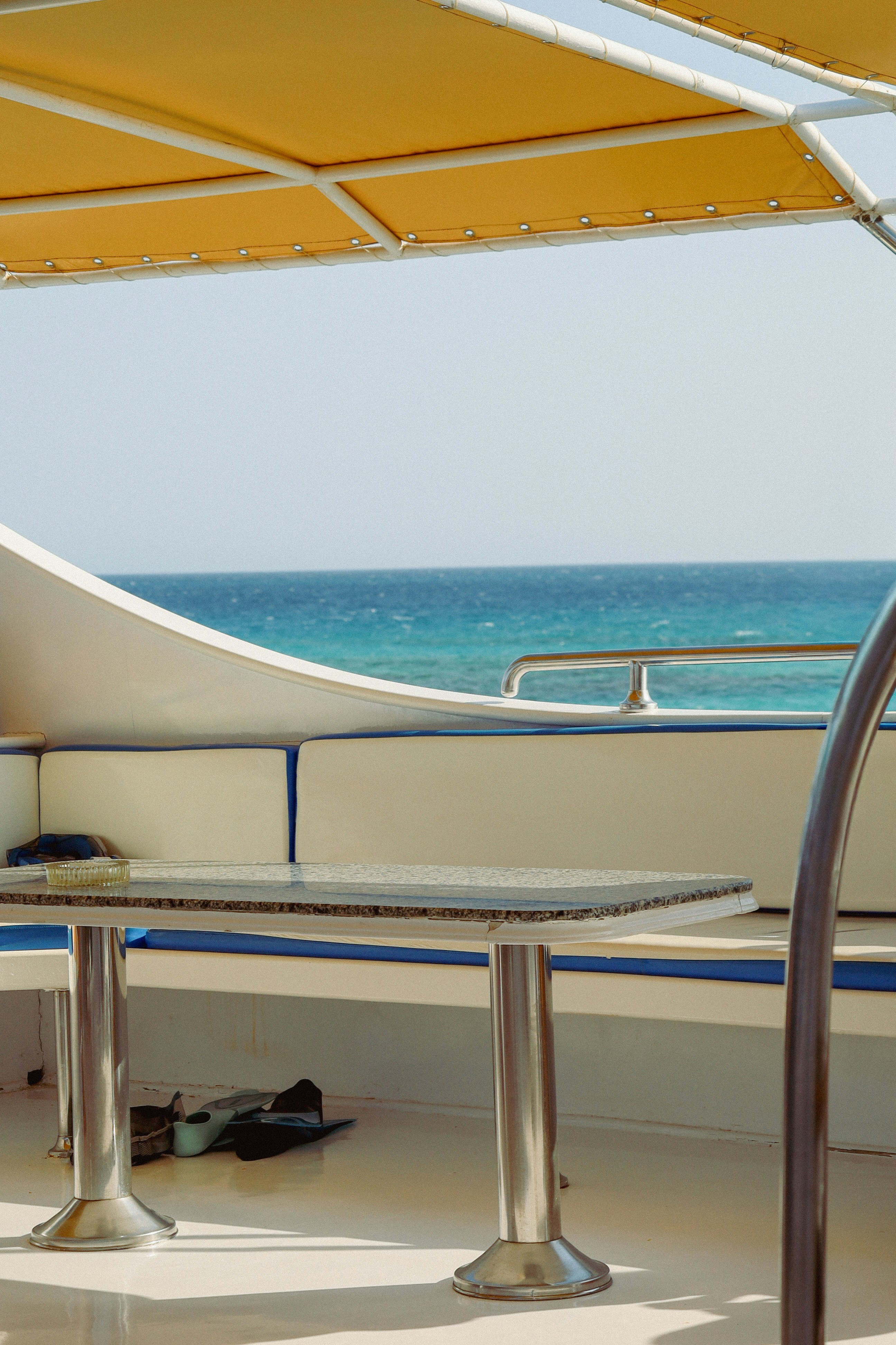 View from the shaded deck of a boat on the Red Sea, with cushioned seating, a small table, and turquoise water stretching out to the horizon under a clear sky.