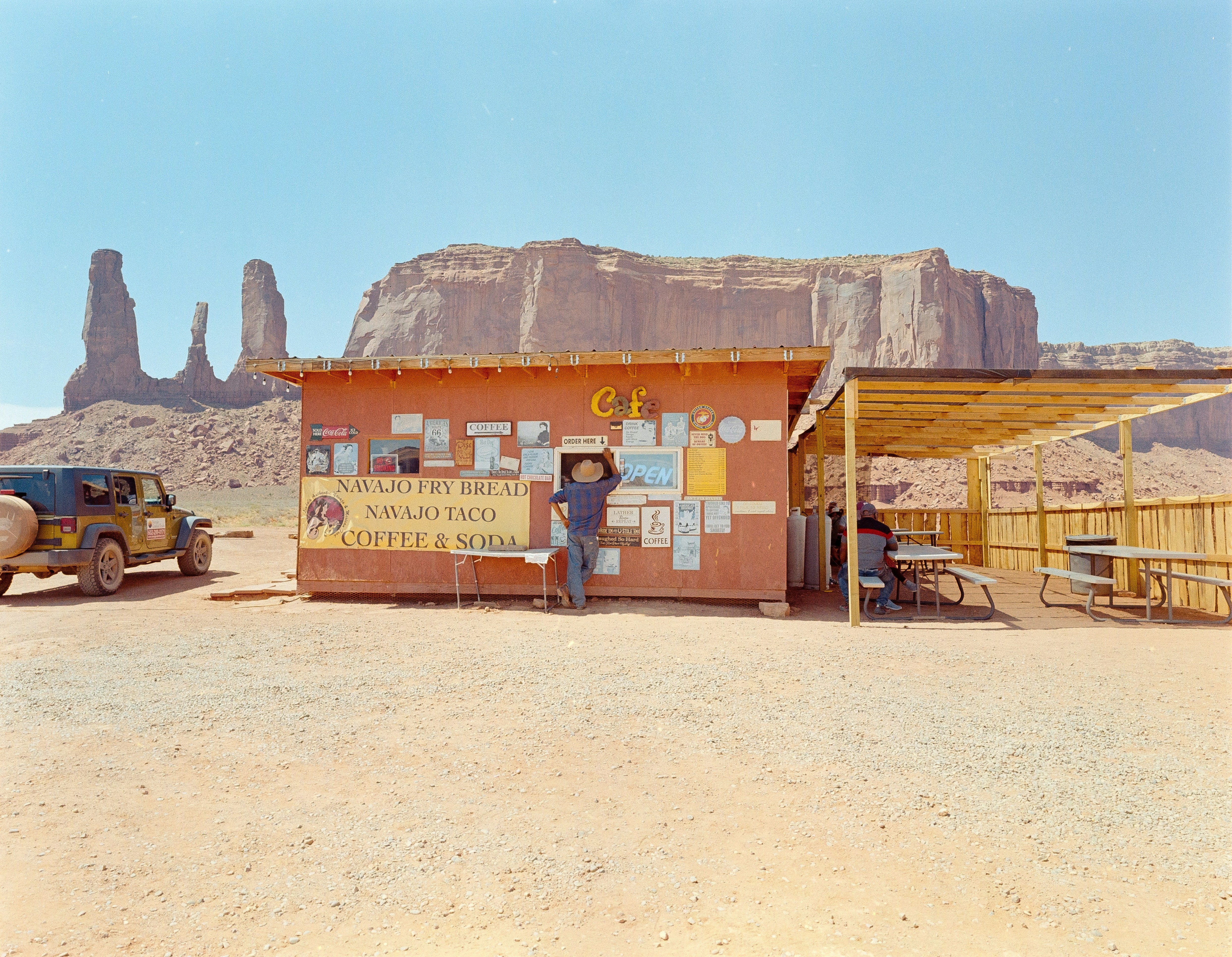 Small roadside café in Monument Valley with a sign advertising Navajo fry bread and tacos, set against dramatic red rock formations under a clear desert sky.